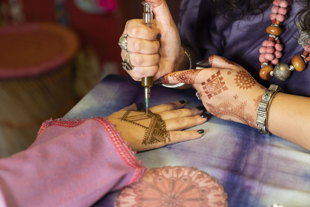 handen beschilderd met henna houden een spuit vast en versieren daarmee een hand iemand anders met een hennapatroon